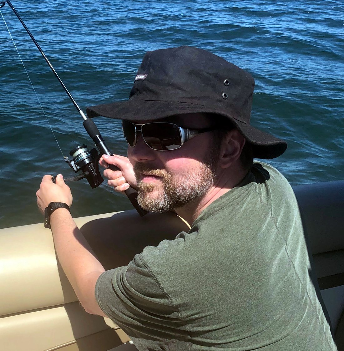 The site's operator on a boat in a bucket hat and sunglasses, holding a fishing rod, face partly shaded