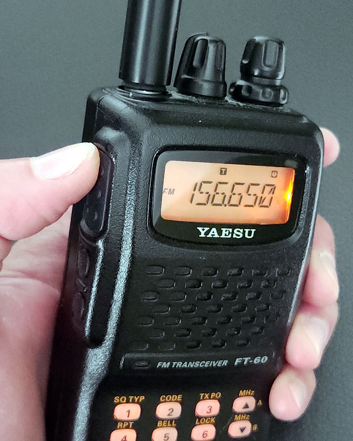 Yaesu FT-60 dual-band handheld radio held in one hand, display lit