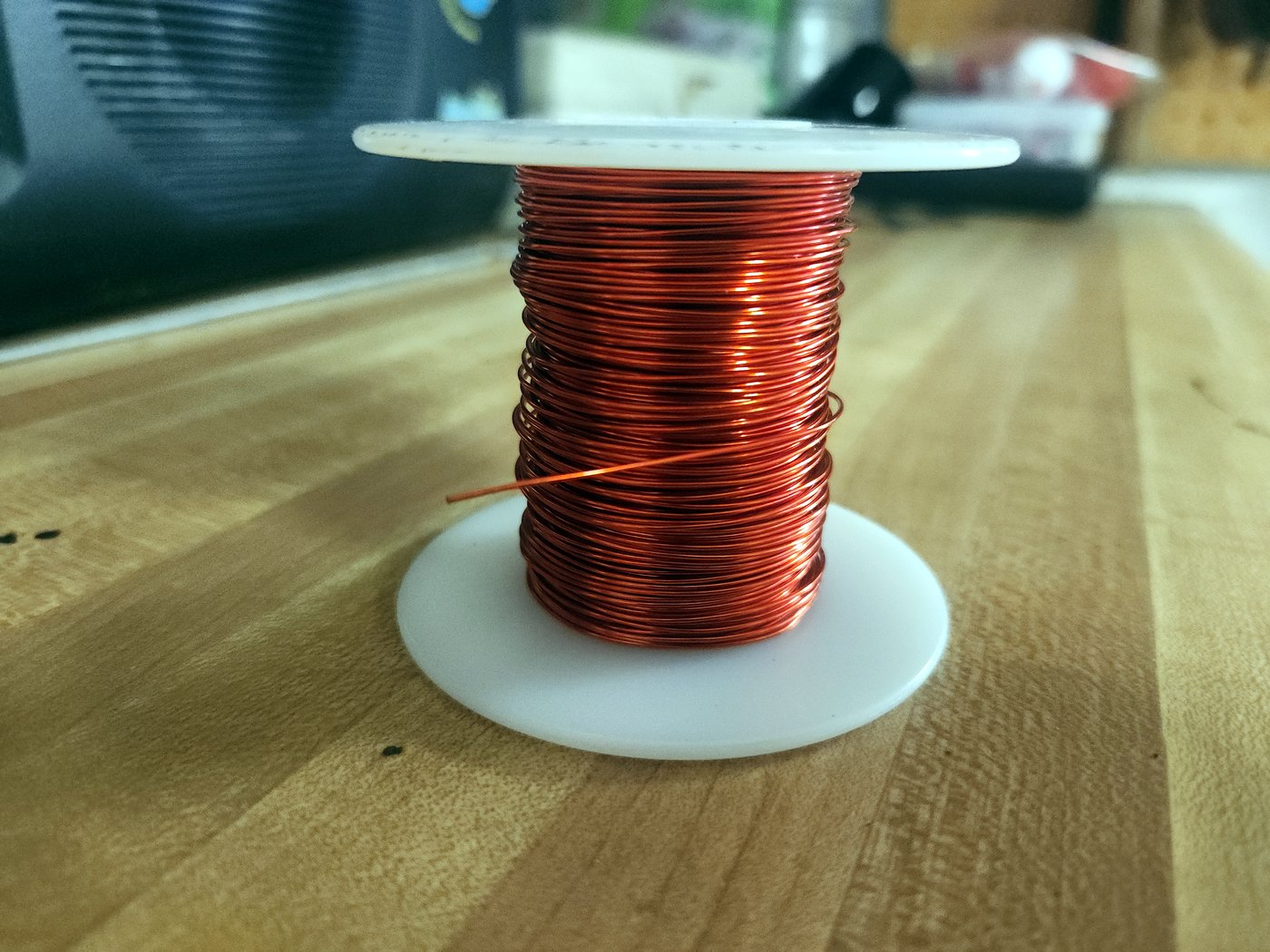 A spool of red enameled 22 AWG copper magnet wire standing on a wooden workbench
